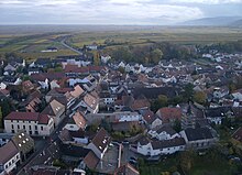 Südlicher Ortsteil, dahinter die Rebenlandschaft des Weinbaugebiets Pfalz mit der Deutschen Weinstraße, am rechten oberen Bildrand die Haardt