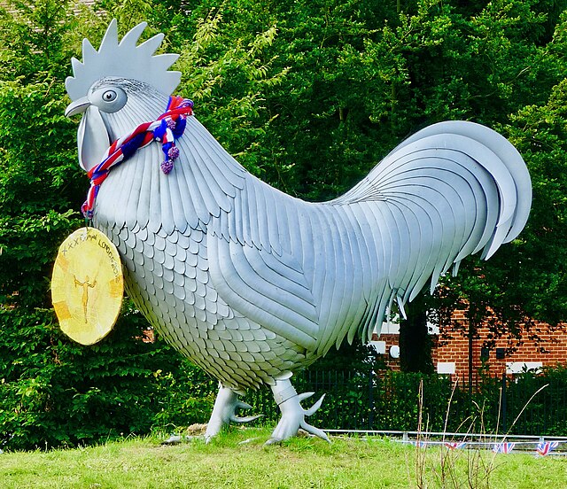 The sculpture, facing left, wearing a gold medal labeled "London 2012" with a red and blue knitted ribbon