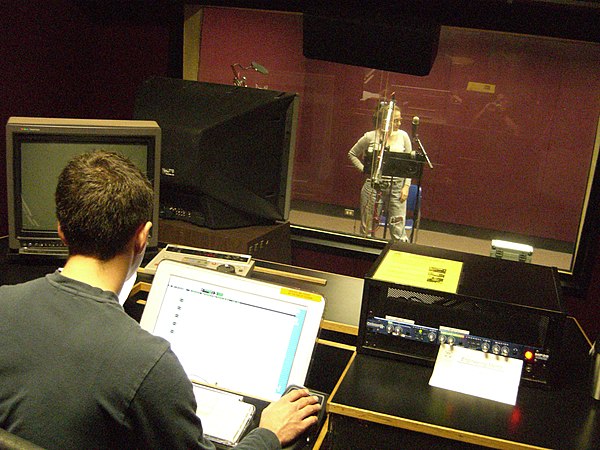 An audio engineer (foreground) recording a voice actor (at microphone) for an animated video production. Lip synchronization of this recording with an