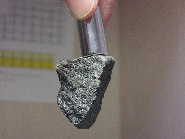 A magnetite rock is being pulled by a neodymium magnet on top.