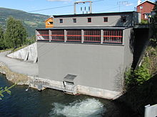 Bâtiment industriel gris avec des lignes électrique le long d'une rivière.