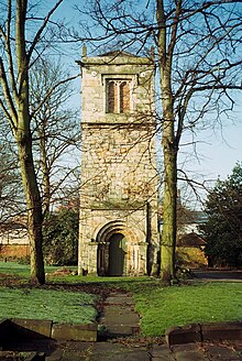 A tower with a round-arched doorway at the bottom, two-light bell openings at the top, surmounted by a low pyramidal roof