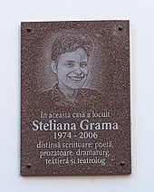 Placă de marmură cu chip de femeie imprimat, și cu textul „În această casă a locuit Steliana Grama, 1974–2006, distinsă scriitoare, poetă, prozatoare, dramaturg, textieră și teatrolog”