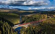Foto eines Zugs auf einer steinernen Brücke, die in einer bewaldeten Landschaft einen Fluss überquert