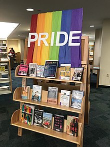 Illustration du Rainbow Book Month par un présentoir de livres sur le thème pour la Pride LGBTQ+ 2017, surmonté d’une tenture arc-en-ciel marquée « pride », à la bibliothèque publique Barbara S. Ponce de Pinellas Park en Floride.