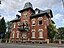 Residential building from 1899 with clinker facade, balcony with wrought-iron railing and tower with Mansard roof. On the right edge of the picture, t...