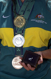 Australian cyclist Lyn Lepore shows a gold, silver and bronze medal from the 2000 Sydney Paralympic Games plus the diamond pin presented to her by BHP for winning gold. 291000 - Paralympic gold silver bronze medals BHP diamond pin - 3b - 2000 Sydney medal photo.jpg