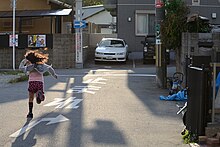 A girl running on a street in Osaka; it is common to see children walking and playing with their friends in the street or taking the metro by themselves unsupervised in Japan. A girl running at the street in Osaka, Japan; May 2013.jpg
