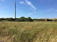 An E-pen at RAF Andreas (2018). These were situated predominately on the eastern and northern side of the airfield and were designed to afford shelter from attack for aircraft and ground crew. Two aircraft could be accommodated within the pen. Today, this one houses a mobile phone mast. E pen RAF Andreas.jpg