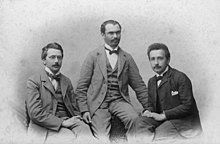 Сидят трое молодых людей в костюмах с высокими белыми воротниками и галстуками-бабочками. 