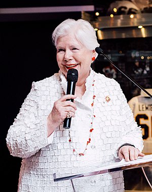 Dowdeswell wearing white holding a microphone at Hockey Hall of Fame in Toronto.