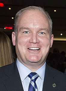 Photograph of O'Toole smiling. He is wearing a dark blue suit with a Canadian lapel pin.