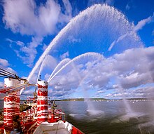 Onboard view of Fireboat John J. Harvey in Tauba Auerbach dazzle camouflage performing a water pumping demonstration in Oyster Bay, New York with artificial rainbow visible Fireboat John J. Harvey at Oyster Bay NY Oyster Festival 2018.jpg