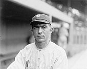 A man wearing a white baseball jersey and a dark crownless baseball cap with an interlocking white "NY" on the face