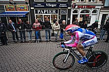 A man riding a bike while wearing a blue, white, and pink skinsuit.