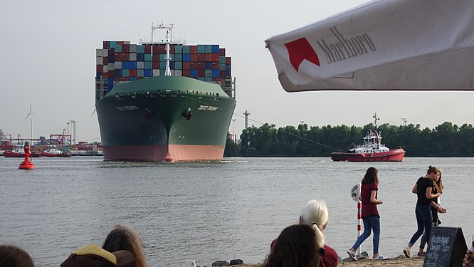 Close to Hamburg's Elbe beach, a container ship is pulled out of the harbour basin by tugboats