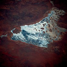 Fotografía satelital de una masa de agua de forma irregular, que contiene numerosas islas pequeñas y está rodeada de tierra roja marcada por numerosas líneas paralelas.