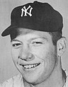 A black and white headshot of a youthful, white baseball player, smiling at the camera, wearing a Yankees baseball cap.