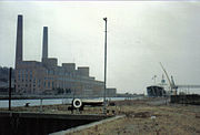 Large building with two chimneys seen across a dock with one boat moored.