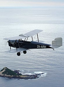 Fotografía de un espartano de tres plazas volando sobre el agua con un punto de tierra en el fondo