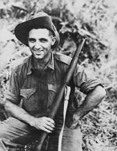 A portrait of Tom Derrick in military clothing with a rifle in his hand