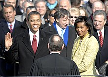 Fotografía de Obama levantando su mano izquierda frente a una multitud de personas.