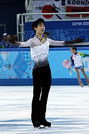 Hanyu steht mit ausgebreiteten Armen, zu einer Verbeugung ansetzend, in der Mitte der Eisfläche. Sein Kostüm besteht aus einem weißen, mit buntem Strass besetzen Hemd, einer schwarzen Hose und schwarzen Handschuhen. Im Hintergrund ein Blumenkind vor die Bande im Design der Olympischen Spiele in Sotschi, dahinter vor der Publikumstribüne ein unterstützendes Transparent.
