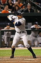 A man in a grey baseball uniform with a navy helmet prepares to swing at a pitch.