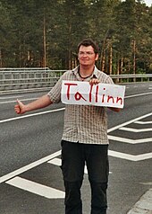 A man with an outstretched thumb and a sign indicating his destination. Alwin Tallinjpg.jpg