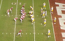 American football players in formation on a green field with the end zone visible.