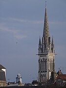 Fotografia colorida de uma torre de igreja projetando-se acima dos telhados.