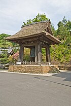 Farvefoto af klokketårnet i et buddhistisk tempel under en overskyet blå himmel.