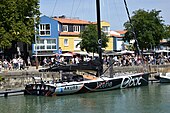 Vu de trois quarts arrière, en entier, voilier noir et argenté, amarré au quai.