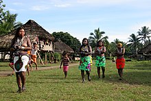 Cuatro mujeres, con faldas de colores, y un niño al aire libre.