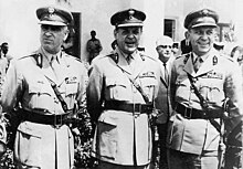 Georgios Papadopoulos stands in military uniform, flanked by two other men in uniform