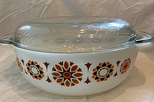 A white oval dish decorated with stylized orange, red and black flowers with a clear lid.