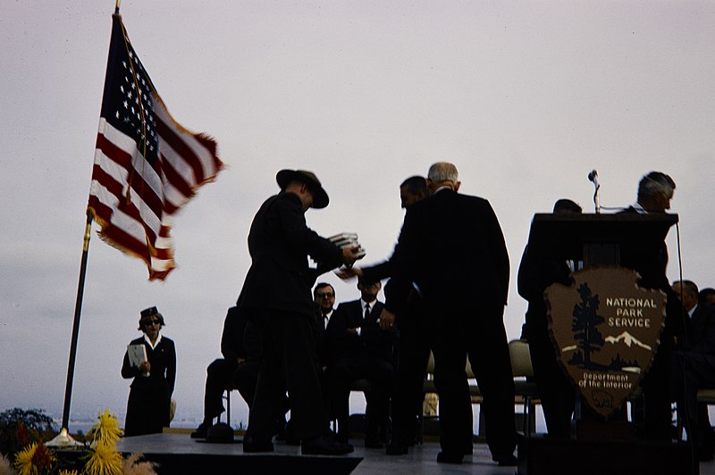 File:Ranger passing books to another man on stage with the NPS arrowhead on the microphone stand in Cabrillo National Monument. (8b7efd7949074830b3085a662ac2e96c).jpg