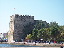 Foto van een hoog, ruwweg vierkant stenen fort in een moderne kuststad.