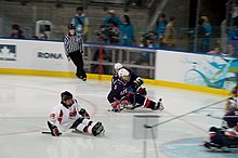 In-game action photo of sled hockey players propelling themselves with sticks