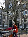Woman, biking over the bridge in Amsterdam city, with old facades in the background; free photo Fons Heijnsbroek, 2022-01.jpg