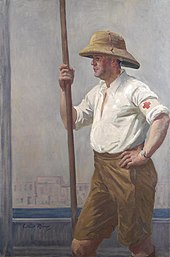 A three-quarter length portrait of a Red Cross and Order of St John barge orderly, wearing sandy coloured shorts, pith helmet and white shirt. He stands side on and holds a wooden barge pole in his right hand. He appears to be standing on the deck of a boat, with the River Tigris and buildings on the riverbank visible behind him, 1919. A Brcs and Osjj Hospital Barge Orderly on the Tigris Art.IWMART3839.jpg
