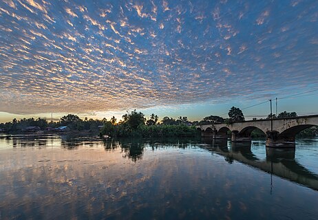 Bridge to Don Khon seen from Don Det with water reflection of stringy orange clouds at sunrise in Laos