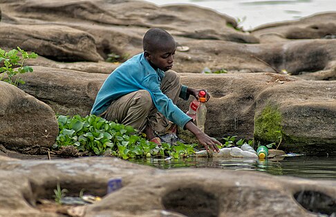 A young boy picks up plastic bottles on the banks of the River Benue. Plastic is the biggest polluter of the world’s oceans and due to its composition it takes a long time to degrade hence creating greenhouse gasses which warm up the world. Photo by Ummigarba