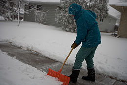 A person shoveling snow off of a sidewalk using a snow shovel