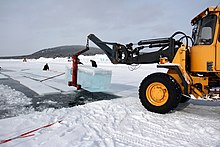 Photographie d'un véhicule soulevant un bloc de glace hors de l'eau dans un paysage recouvert de neige