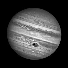Photo noir et blanc : un cercle noir (l'ombre de Ganymède) est visible au milieu de la Grande Tache Rouge de Jupiter