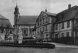 Historické černobílé foto, v popředí náves se svatojánskou sochou, za ní zleva fara, kostel a hostinec