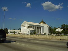 Large Greco-Roman style church sitting along a road within a residential area.