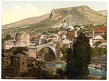 Stari Most, a UNESCO World Heritage Site and monumental Serbian Orthodox Cathedral of the Holy Trinity (white church in the background) were destroyed by Croat forces in the Bosnian War, but were later rebuilt. Mostar1890-1900.jpg