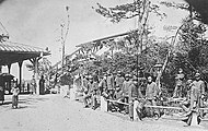 桶川停車場の従業員と駅前にあった小公園。当時の駅舎や跨線橋も見える。（1907年頃）[5]